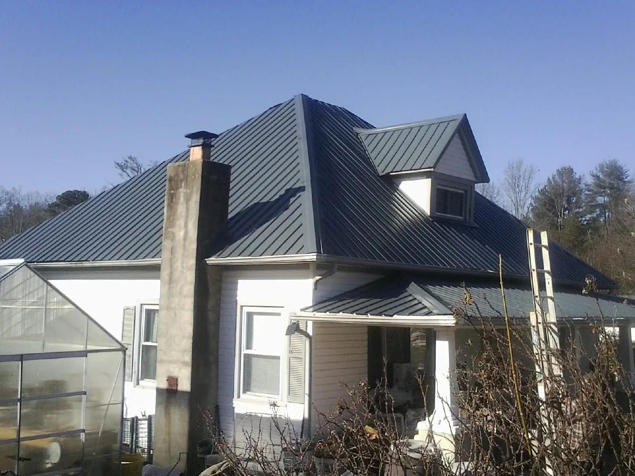 Dark blue standing seam metal roof on a white farmhouse with dormer — Slate & Tile Roof Repair by Roofing Brothers in Eastchester