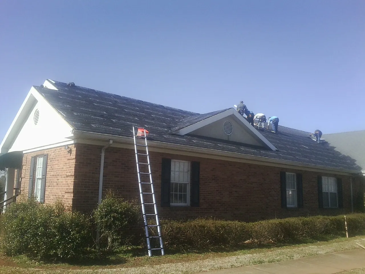 Crew tearing shingles off a brick ranch roof with a ladder set — Emergency Roof Repair work by our crew in Eastchester