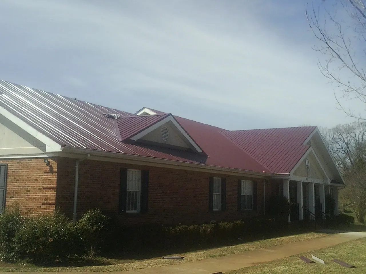 Red metal roof with gabled entries on a long brick building, from a Hail Damage Roof Repair job in Eastchester