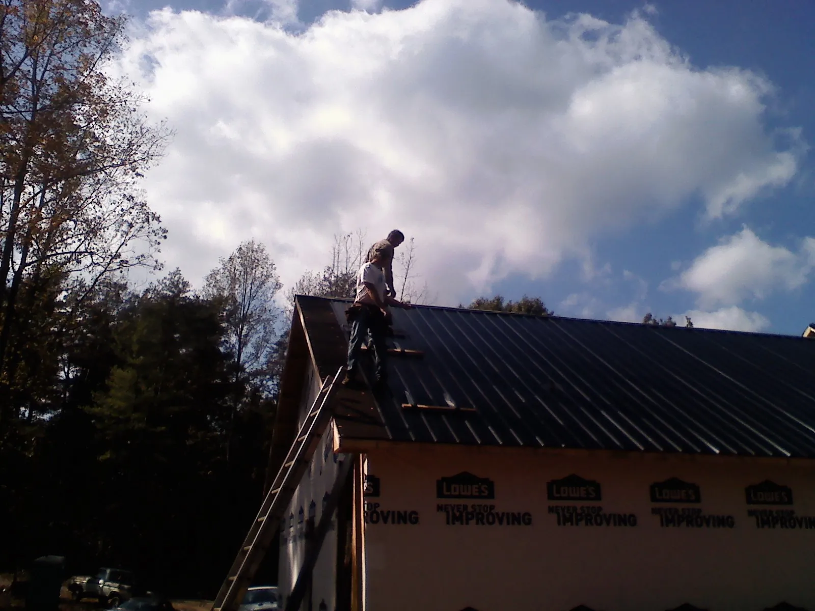 Roofer fastening dark metal panels high against a cloudy sky, from a Roof Inspection job in Eastchester