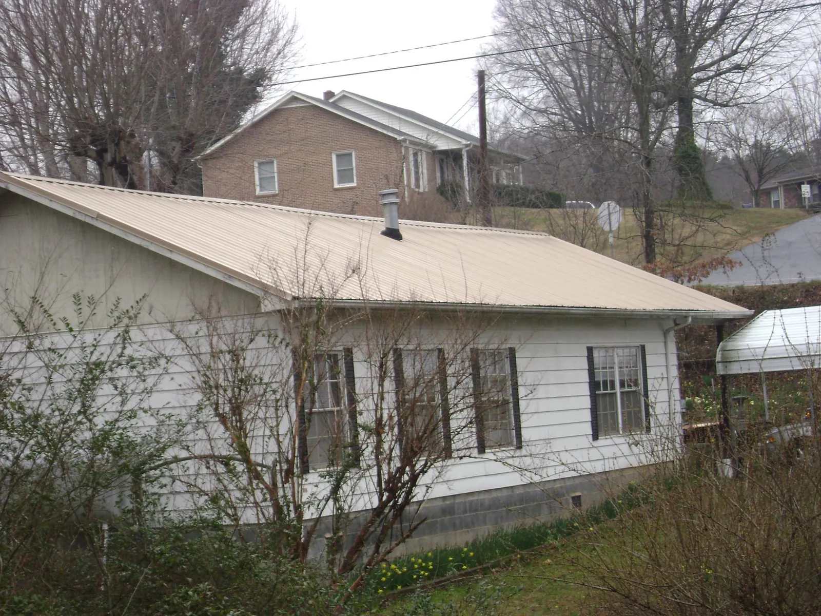 Tan metal roof on a white sided house set into a hillside — Commercial Roofing by Roofing Brothers in Eastchester